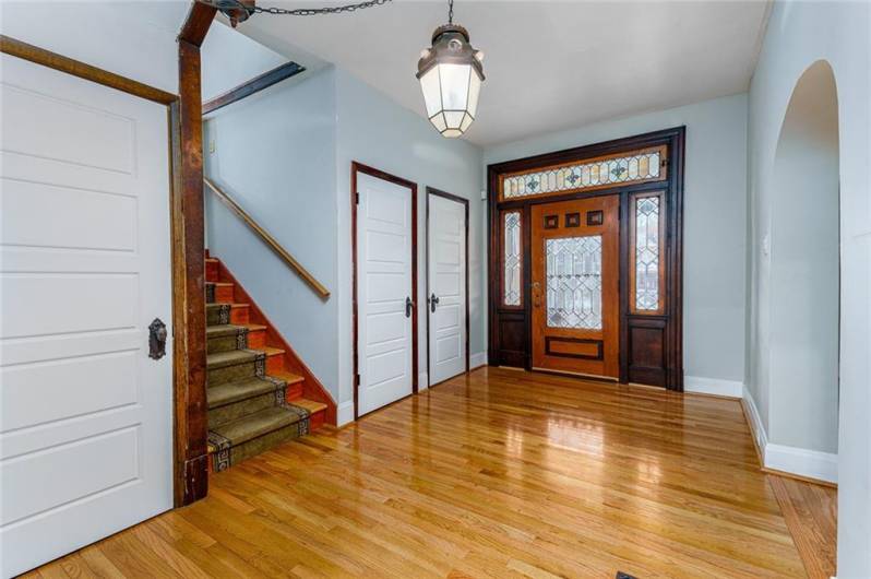 This grand entryway makes a stunning first impression, featuring a gorgeous door with intricate leaded glass, framed by matching leaded glass panels that fill the space with natural light and timeless elegance. The rich hardwood floors enhance the warmth and character of the space, creating an inviting atmosphere that sets the tone for the rest of the home. Spacious and welcoming, this entry is both a statement of beauty and a perfect introduction to the home's charm.