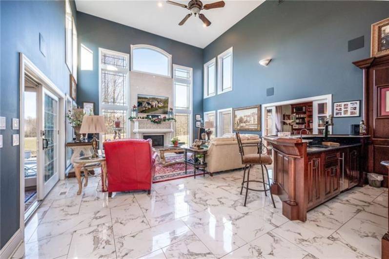 Dramatic 2 Story Family Room With Floor to Ceiling Windows and Stone Fireplace.  This room open up (on left), to an All Season Glass Sunroom.  Jim Trenga, an amazing Craftsman, constructed the Wet Bar with imported Black Antique Leather Granite.