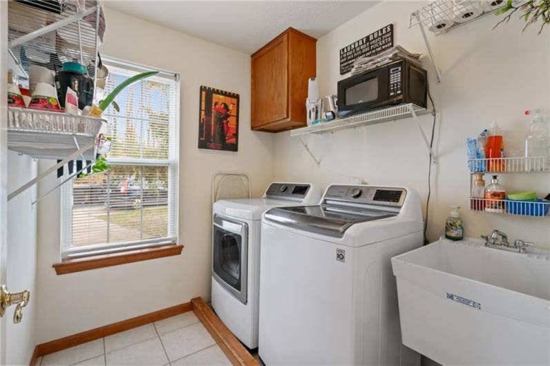 The spacious laundry room offers tiled floors an oversized window, built-in shelving, and a stationary tub.