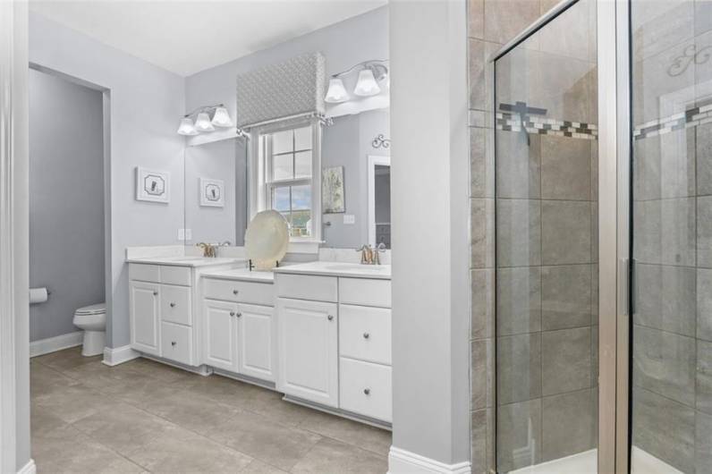 The Primary Suite bath includes his/her sinks, a vanity area and a tile shower with glass enclosure.