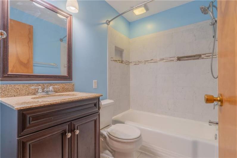 The neutral updated hall bath includes ceramic floors,  an updated tiled shower and a newer vanity.
