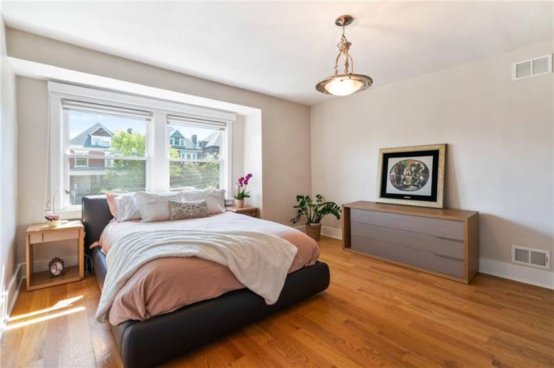The primary bedroom is brightly illuminated by day thanks to the large windows (with blackout shades to ensure peaceful sleep). A large custom closet stretches along the wall opposite the windows (not pictured)