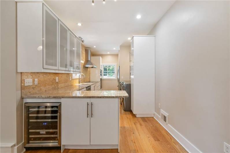 A modern kitchen with sleek white cabinets, granite counters, travertine tile backsplash (and a wine cooler)