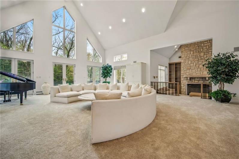 Bathed in natural light from soaring windows, the expansive living area offers a sophisticated retreat with a grand piano, a striking stone fireplace, and seamless access to the outdoors.