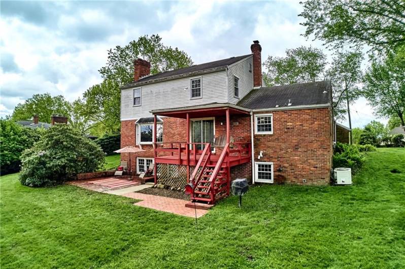 Rear view of the home shows the brick patio, covered deck, and nicely landscaped yard.