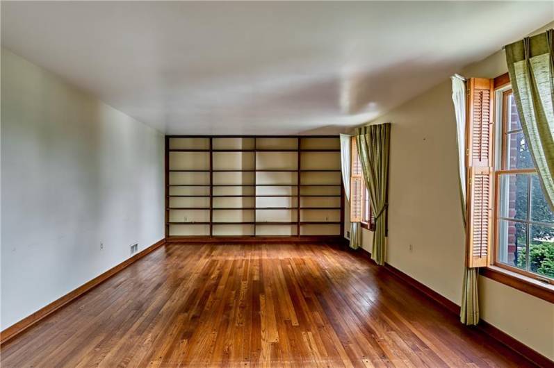 The Living Room features a beautiful hardwood floor, built in shelves, and two large windows with shutters.