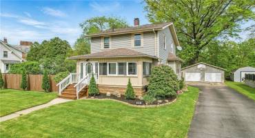 Charming two-story home features a neatly manicured lawn, a cozy enclosed porch, and a detached two-car garage with a basketball hoop.