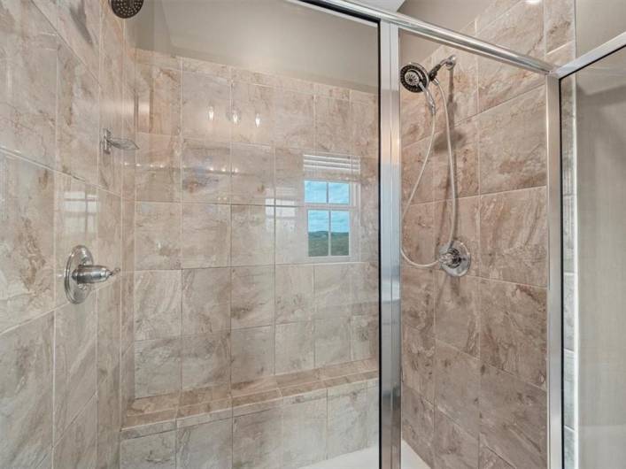 This luxurious walk-in shower showcases elegant floor-to-ceiling tile with rich, natural stone patterns that add warmth and sophistication. Featuring dual showerheads and sleek glass doors, the design offers both functionality and style.