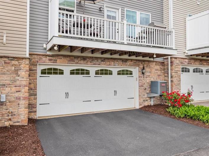 This townhome features a spacious two-car garage with charming carriage-style doors and decorative windows, offering both functionality and curb appeal. The brick façade adds a touch of elegance and durability, while the overhead balcony provides outdoor living space directly above. A freshly paved driveway and neatly landscaped garden bed complete the exterior, making for a well-maintained and welcoming entrance to the home.