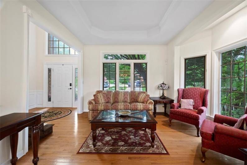 This living room’s bay window frames serene views while the tray ceiling elevates every gathering with classic charm and grace