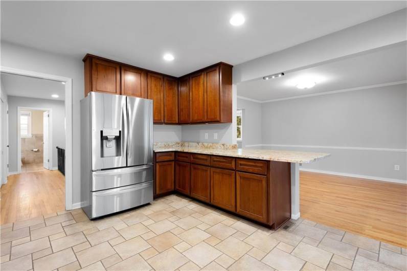 The kitchen showing a large stainless steel French door refrigerator, corner cabinetry, and a peninsula counter that opens to an adjacent dining space with hardwood flooring. Recessed lighting enhances the clean and bright atmosphere.
