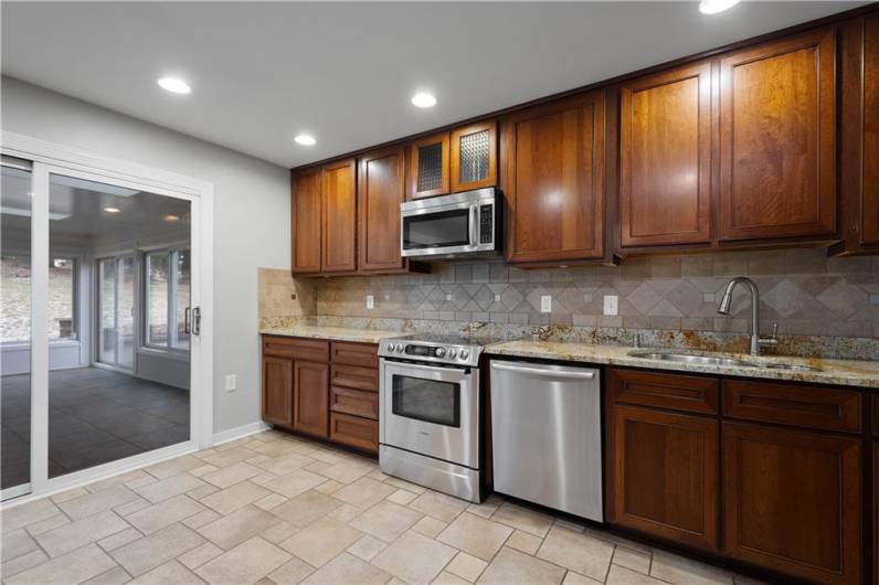 Another angle highlighting the cooking and sink area. The image shows a sliding glass door leading to a sunroom, bringing natural light into the kitchen and offering a seamless indoor-outdoor connection.
