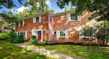A charming Upper St Clair raised ranch red brick home with white shutters and a vibrant red front door.