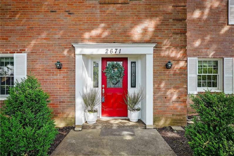 A close-up of the front door area. The red door is framed by sidelights and a small portico with white columns.