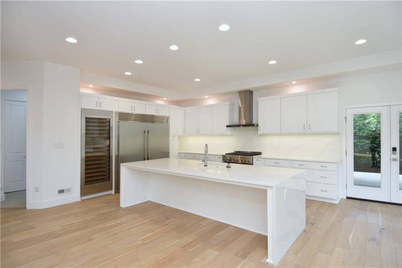 Amazing chef's kitchen featuring a waterfall Quartz Island, Sub-Zero wine fridge, Side by Side Electrolux Refrigerator/Freezer & professional series Jennair convection oven with gas cooktop.
