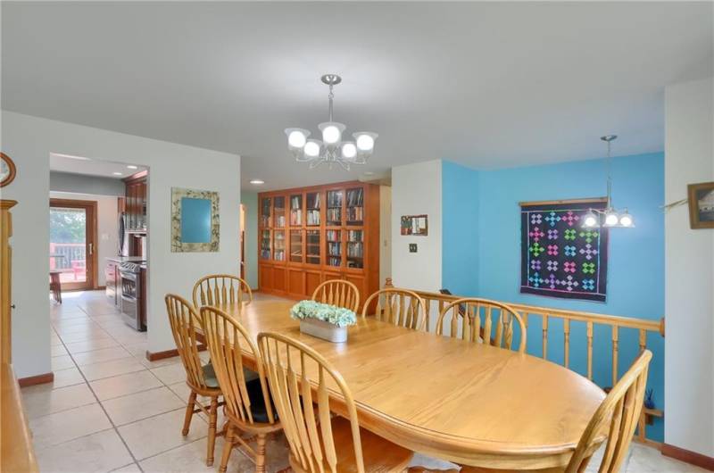 This bright and spacious dining area is perfect for gatherings, featuring tile flooring, modern lighting, and built-in shelving for added charm and functionality. The space flows seamlessly into the kitchen and offers a peek into the lower level below.