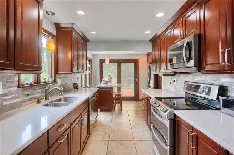 This beautifully updated kitchen is filled with natural light from multiple windows and glass doors, creating a warm and inviting space. Rich cabinetry, sleek quartz counters, and modern stainless appliances add style and function to this bright, cheerful culinary hub.