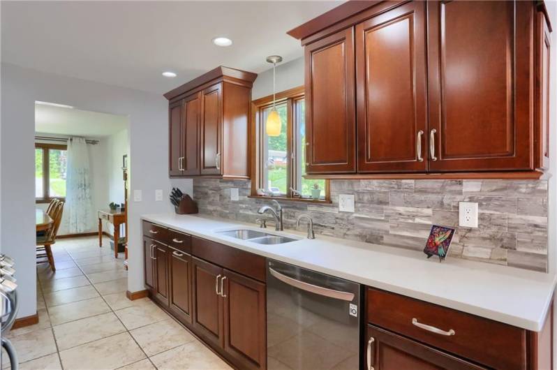 A large window over the sink fills this kitchen with natural light, highlighting the rich cabinetry, sleek quartz counters, and stylish tile backsplash. The layout offers plenty of prep space and a bright, welcoming atmosphere for everyday living.