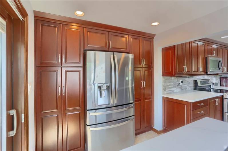 Floor-to-ceiling cabinetry offers abundant storage in this stylish kitchen, perfectly complemented by a sleek French-door stainless refrigerator. The rich wood tones and modern finishes create a polished, functional space for everyday living.