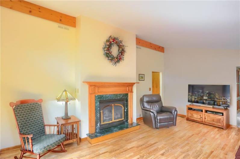 The family room’s cozy focal point is a beautiful gas fireplace framed in rich wood and elegant green marble, adding warmth and charm to the space. Vaulted ceilings and hardwood floors enhance the room's open, inviting feel.