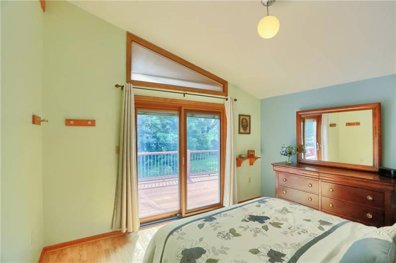 This serene primary bedroom features a vaulted ceiling and transom window that floods the space with natural light. Enjoy peaceful mornings and private access to the deck through the sliding glass doors—perfect for taking in the tranquil backyard views.