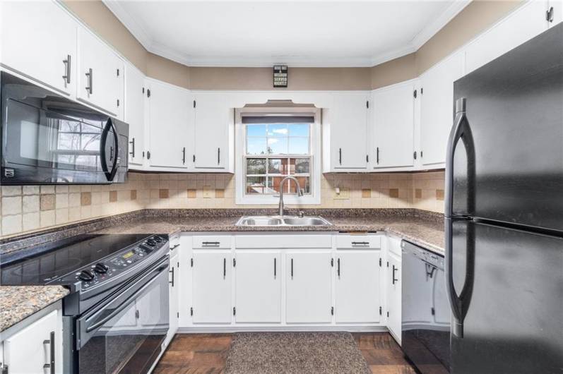Efficient U-shaped kitchen with white cabinetry, modern black appliances, tiled backsplash, and plenty of counter space.