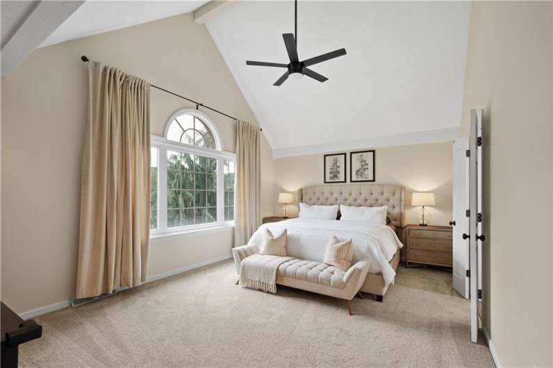The serene primary bedroom features a neutral palette, a soaring cathedral ceiling, and a gentle paddle fan—creating a peaceful retreat to unwind and relax.