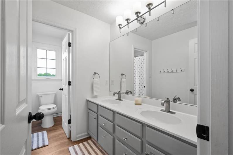 The updated bathroom showcases modern tones, large vanity woth dual sinks, a tub-shower combination, and a separate water closet for added privacy.