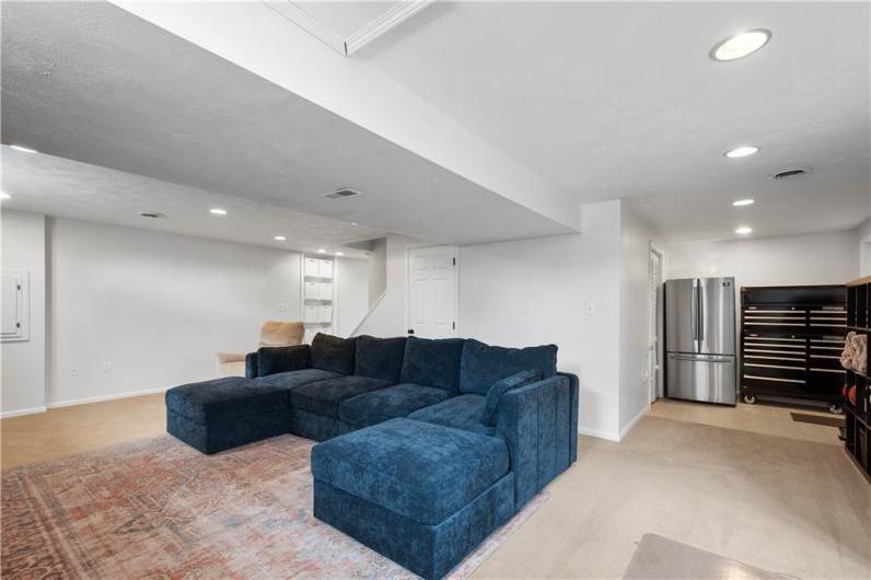The lower-level game room offers ample space for a large sectional sofa, a dedicated spot for a refrigerator, convenient outdoor access, and plenty of storage—perfect for relaxing and entertaining.