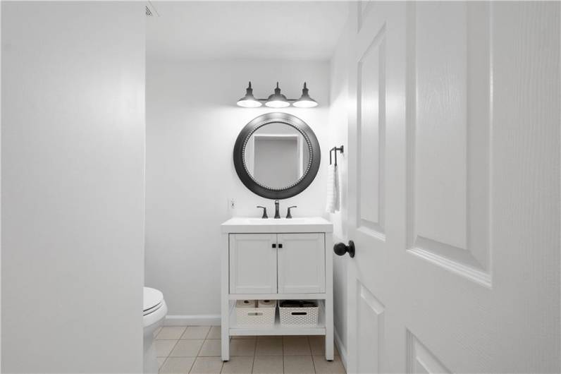 The lower-level powder room features clean white walls, simple tile flooring, and a streamlined vanity for a fresh, uncluttered look.